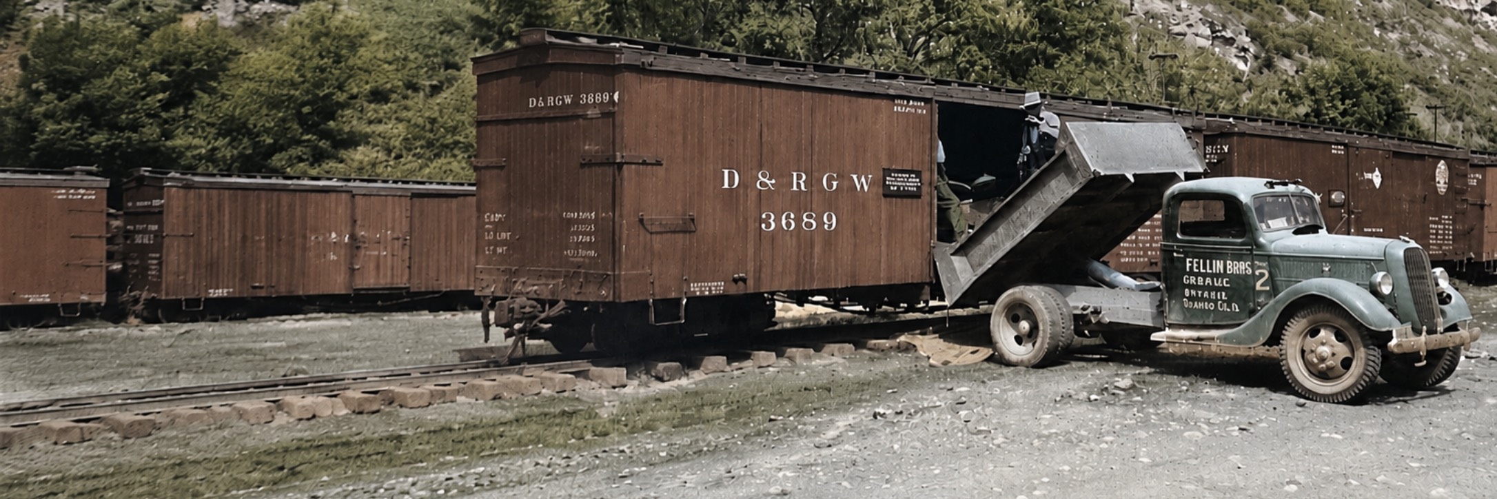 Historic truck unloading material into a railroad freight car in a mountain setting.